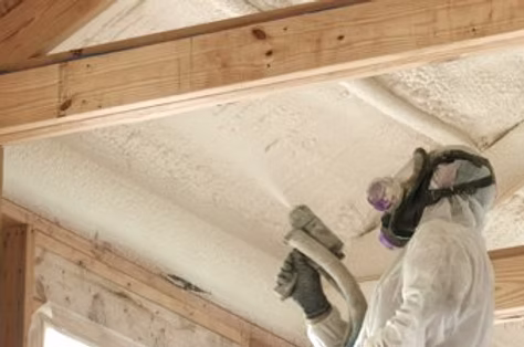 Builder insulating wooden frame house. Close up view of man worker spraying polyurethane foam inside of future cottage, using plural component gun. Construction and insulation concept.